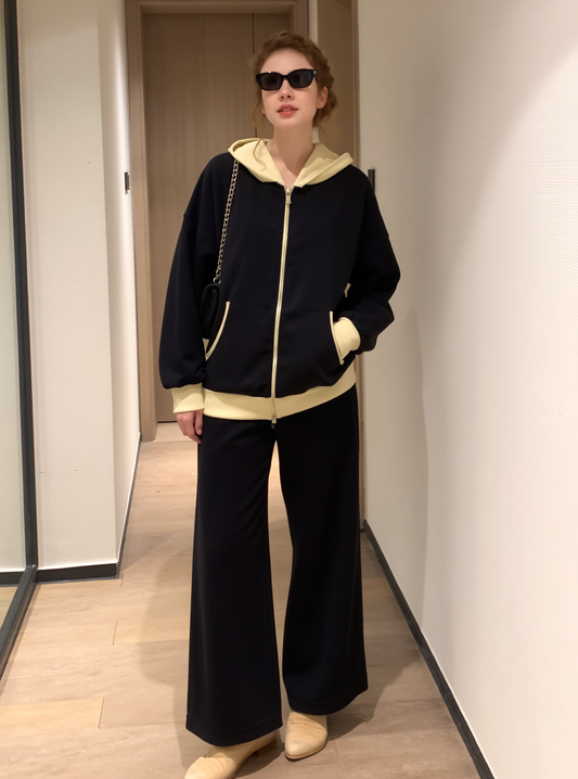 Woman wearing a black zip-up hoodie with beige accents and wide-leg pants, standing indoors.