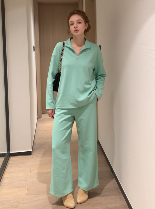 Woman wearing a mint green lounge set with a half-zip top and wide-leg trousers, styled with beige shoes and a black handbag.