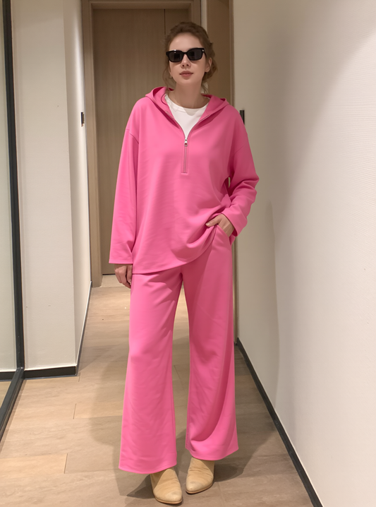 Woman modelling bright pink loungewear set with half-zip hooded top and wide-leg trousers.